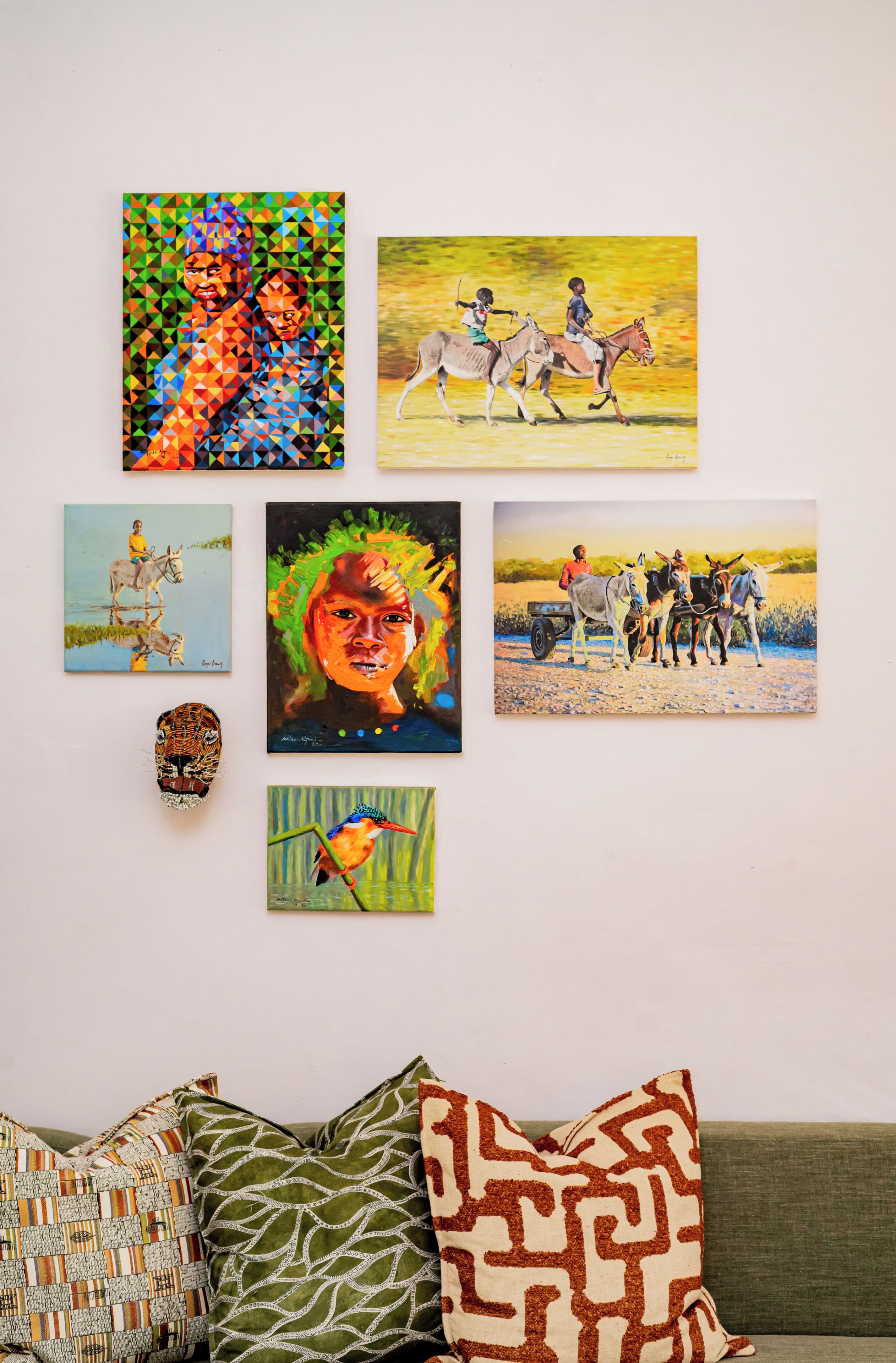 A wall with various artworks and a sofa with patterned cushions.