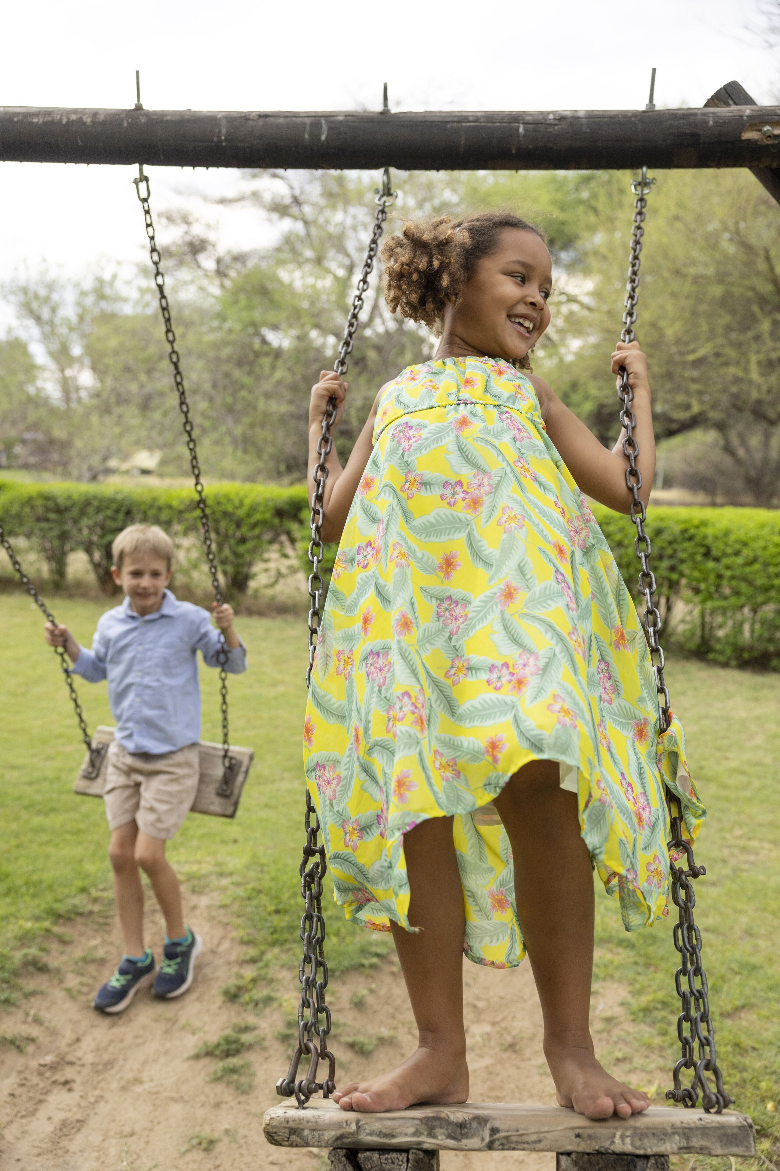 A child on a swing in a park with a grassy area and trees in the background.
