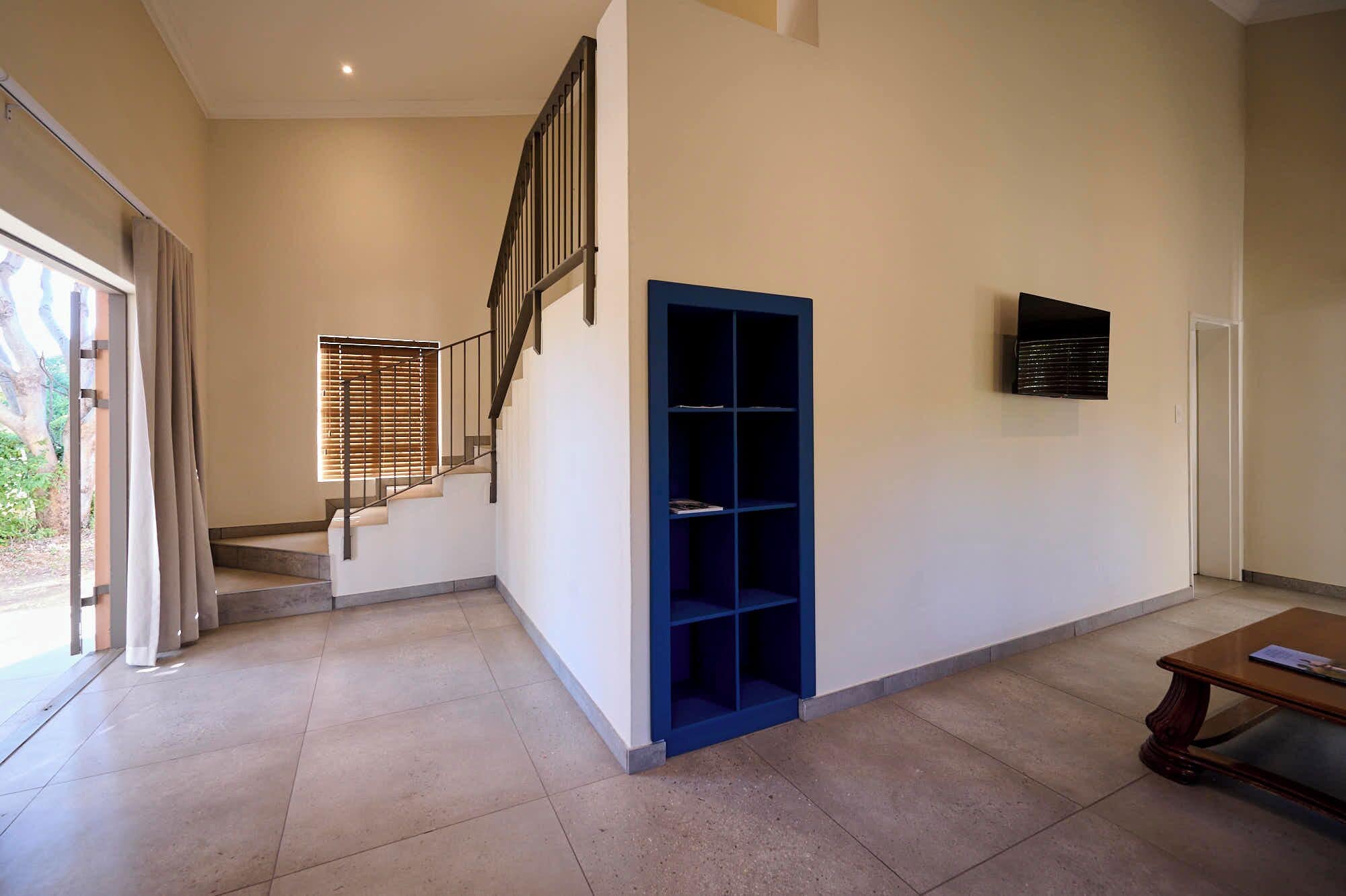 A spacious room with a staircase, a blue shelving unit, and a mounted TV.
