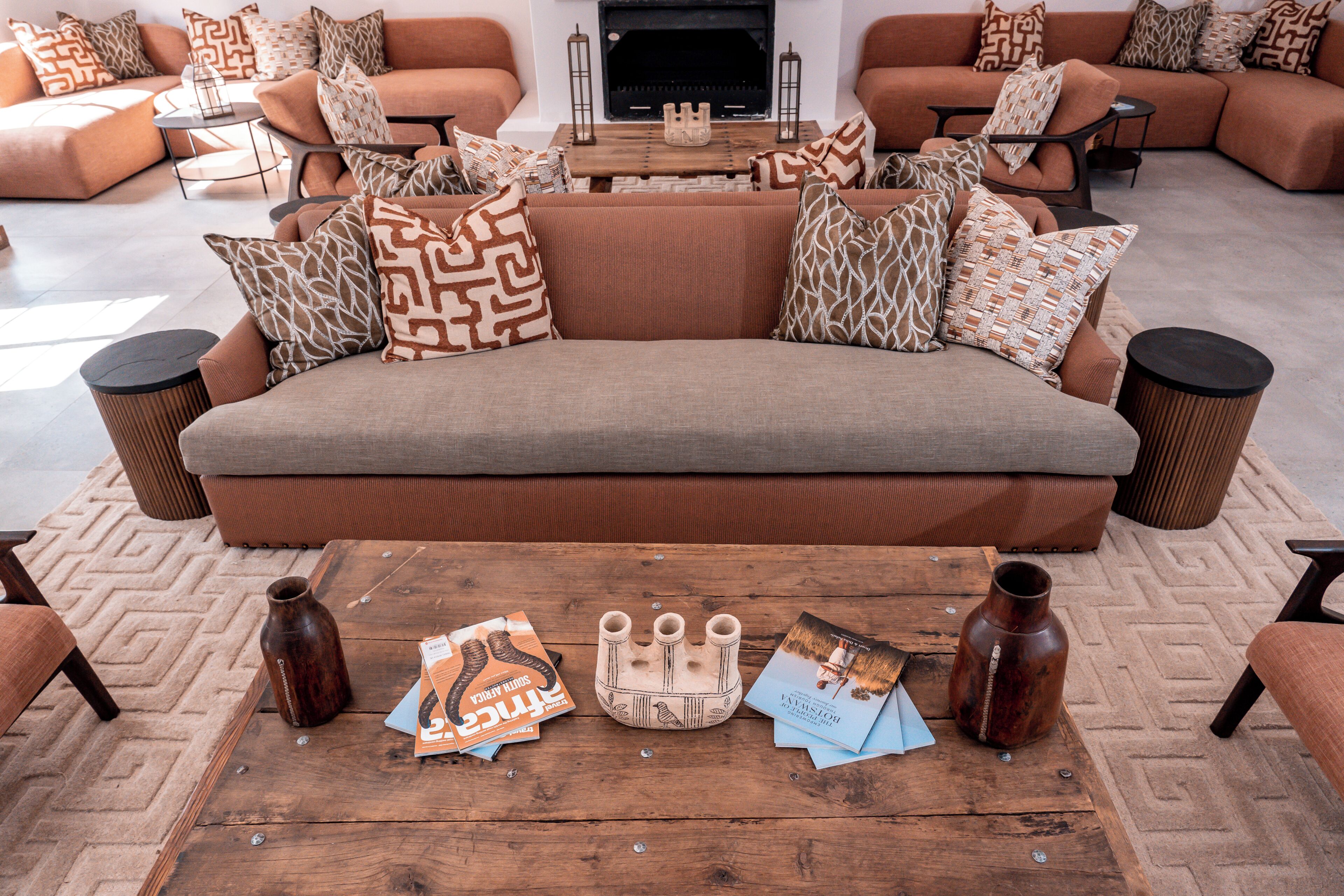 A modern living room with a sectional sofa, patterned throw pillows, a coffee table with magazines and a decorative vase, and a fireplace.