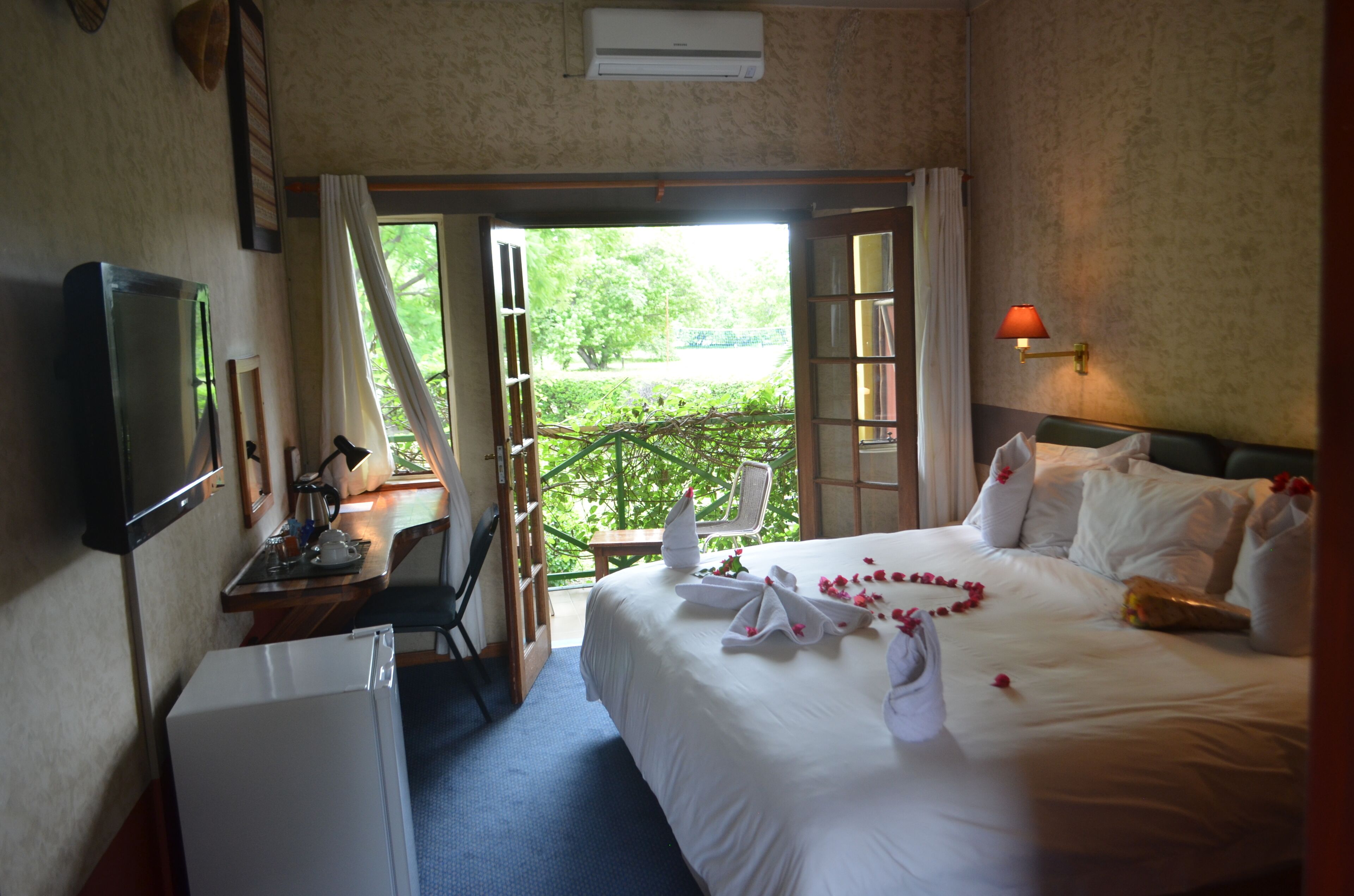 A hotel room with a bed, a desk, a chair, a television, and an air conditioning unit.