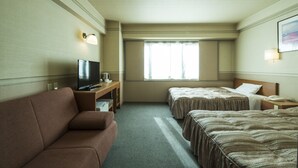 Habitación de hotel con sofá, dos camas, televisor y ventana con cortinas.