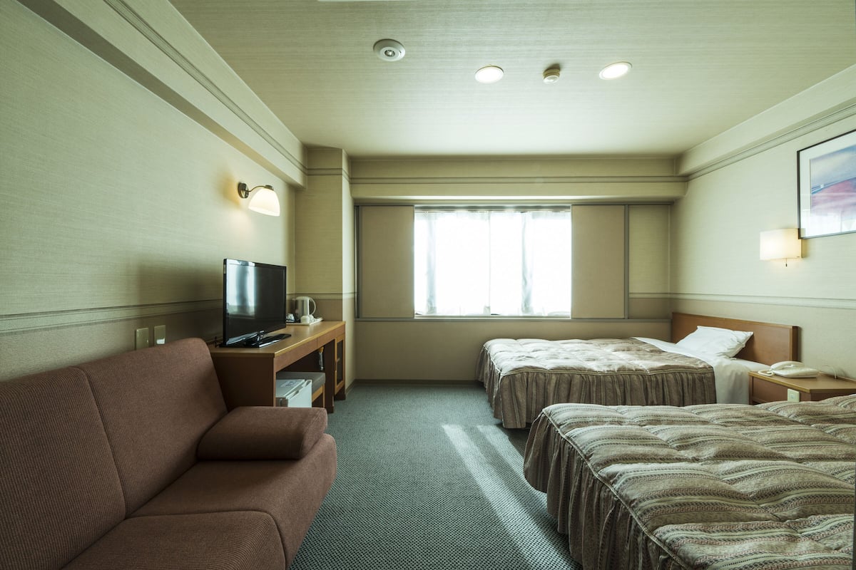 A hotel room with a sofa, two beds, a TV, and a window with curtains.
