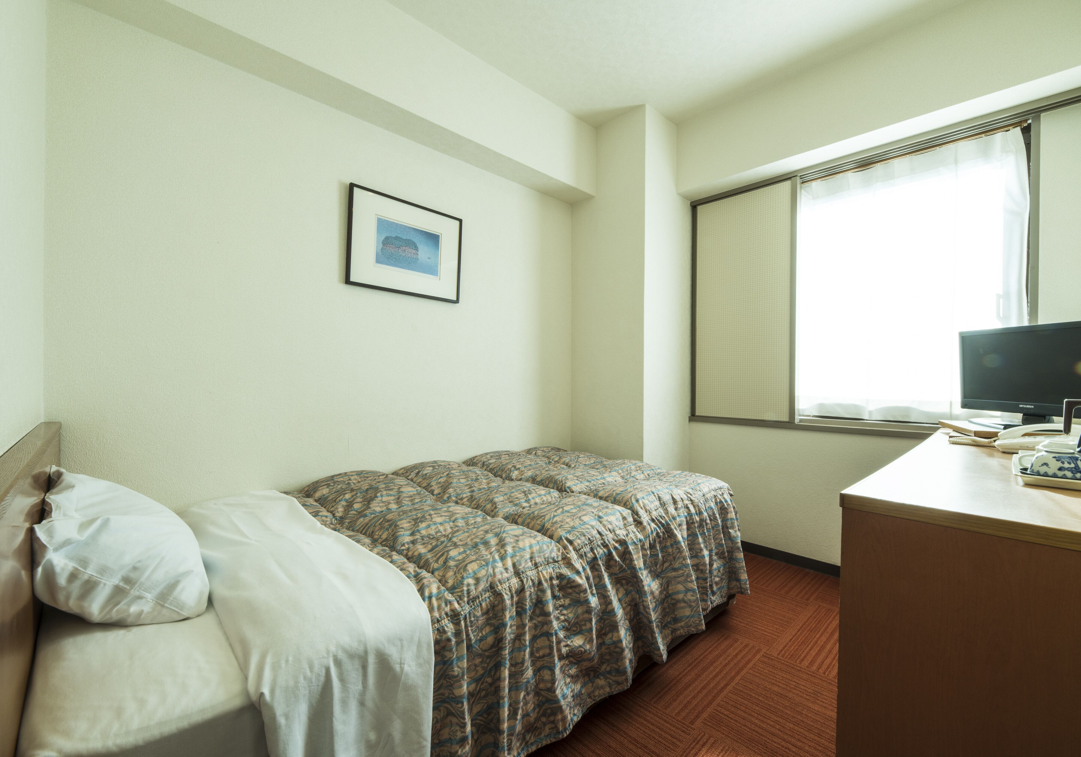 A hotel room with a bed, a desk, a computer, and a window with curtains.
