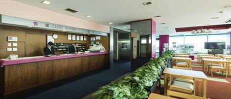 Ett receptionsområde med en bardisk i trä, en skylt som visar vägen till gästrummen och en lång rad med växter.