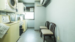 Un cuarto de lavandería con lavadoras, una secadora y dos sillas.