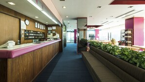 Un área de recepción con un mostrador de madera, una zona de estar con un sofá y una estantería.
