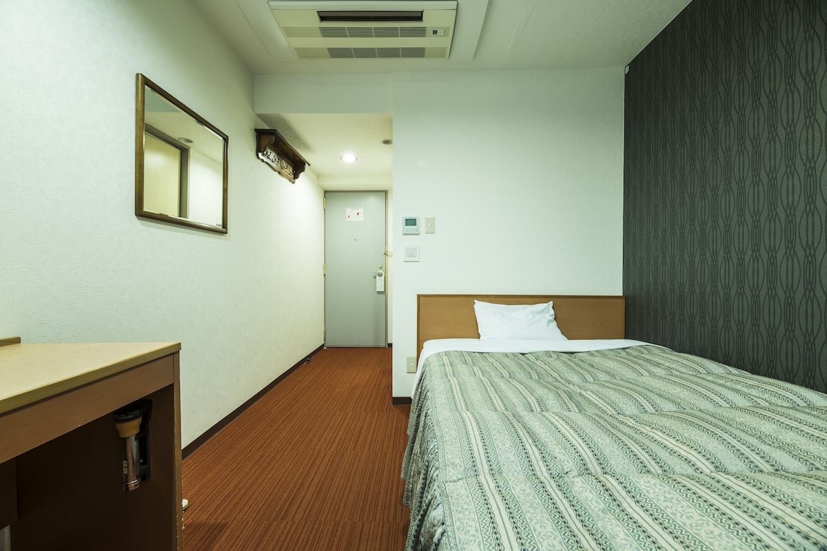 A hotel room with a bed, a desk, a mirror, and a door leading to another room.