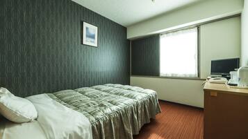 A hotel room with a bed, a desk with a computer, and a window with curtains.
