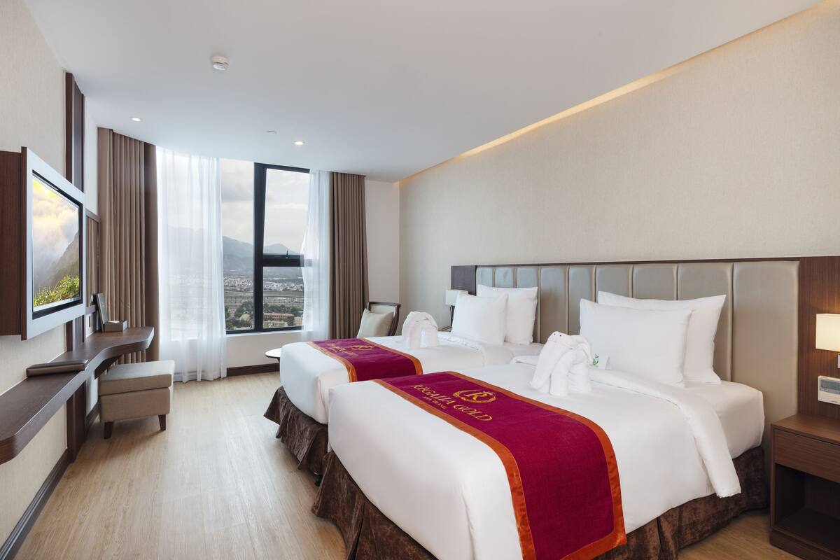 Habitación de hotel con dos camas, televisión, escritorio y un ventanal grande con cortinas.