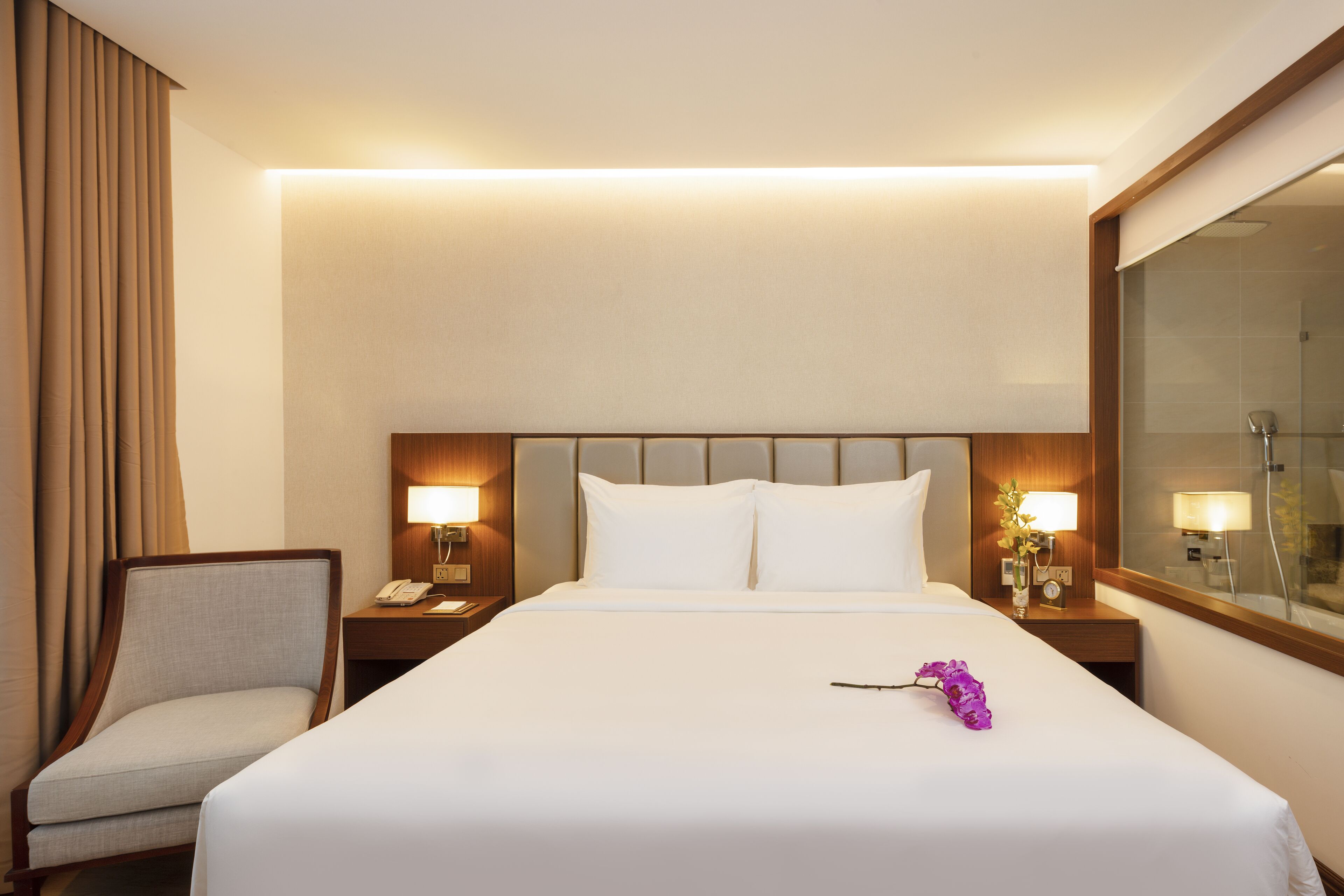 Ein Hotelzimmer mit einem großen Bett, zwei Nachttischen mit Lampen, einem Sessel und einem großen Spiegel.