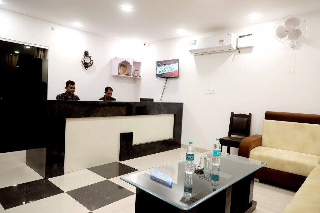 A reception area with a black and white checkered floor, a reception desk, a sofa, and a television displaying 'TEAM INDIA'.