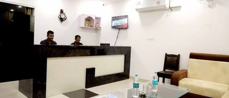 A reception area with a black and white checkered floor, a reception desk, a sofa, and a television displaying 'TEAM INDIA'.