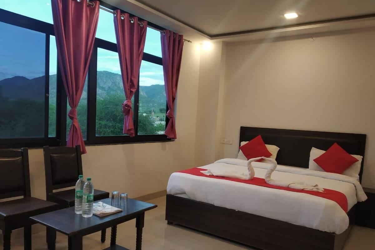 Une chambre d’hôtel avec un lit, une table avec des bouteilles d’eau et une vue sur les montagnes par la fenêtre.