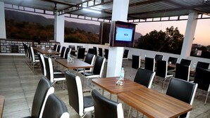 A covered outdoor dining area with tables and chairs, a mounted screen, and a view of the landscape. - Sunrise Palace (Pushkar)