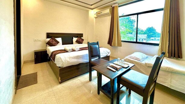 A hotel room with a bed, a desk, and a chair. There is a window with curtains and an air conditioning unit on the wall. - Sunrise Palace (Pushkar)