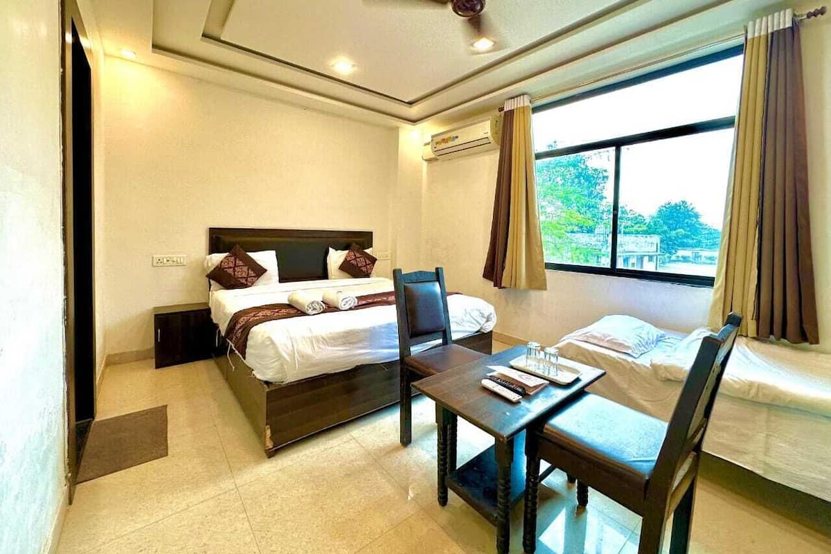 Une chambre d’hôtel avec un lit, un bureau et une chaise. Il y a une fenêtre avec des rideaux et un appareil de climatisation fixé au mur.
