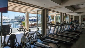 A gym with treadmills, stationary bikes, and an elliptical machine, overlooking a marina with boats and a waterfront view. - 001 Altmore on the Waterfront Marina (Cape Town)