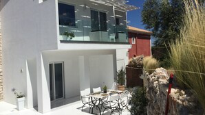 A modern two-story house with a balcony, outdoor seating area, and a stone wall. - Dion Suite And Spa In Zakynthos (Zakynthos)