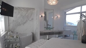 A modern bedroom with a large bed, a bathtub, a vanity with a glass bowl sink, and a large window offering a view of the ocean. - Dion Suite And Spa In Zakynthos (Zakynthos)