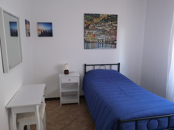 Une chambre à coucher comprenant un lit, un bureau, une chaise, une table de chevet et un mur orné de trois tableaux encadrés.
