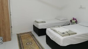 Una habitación pequeña y limpia con dos camas individuales, una puerta de madera, un tapete pequeño y un aire acondicionado de pared.