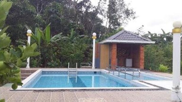 Una piscina rectangular con una estructura pequeña adyacente, rodeada de vegetación.