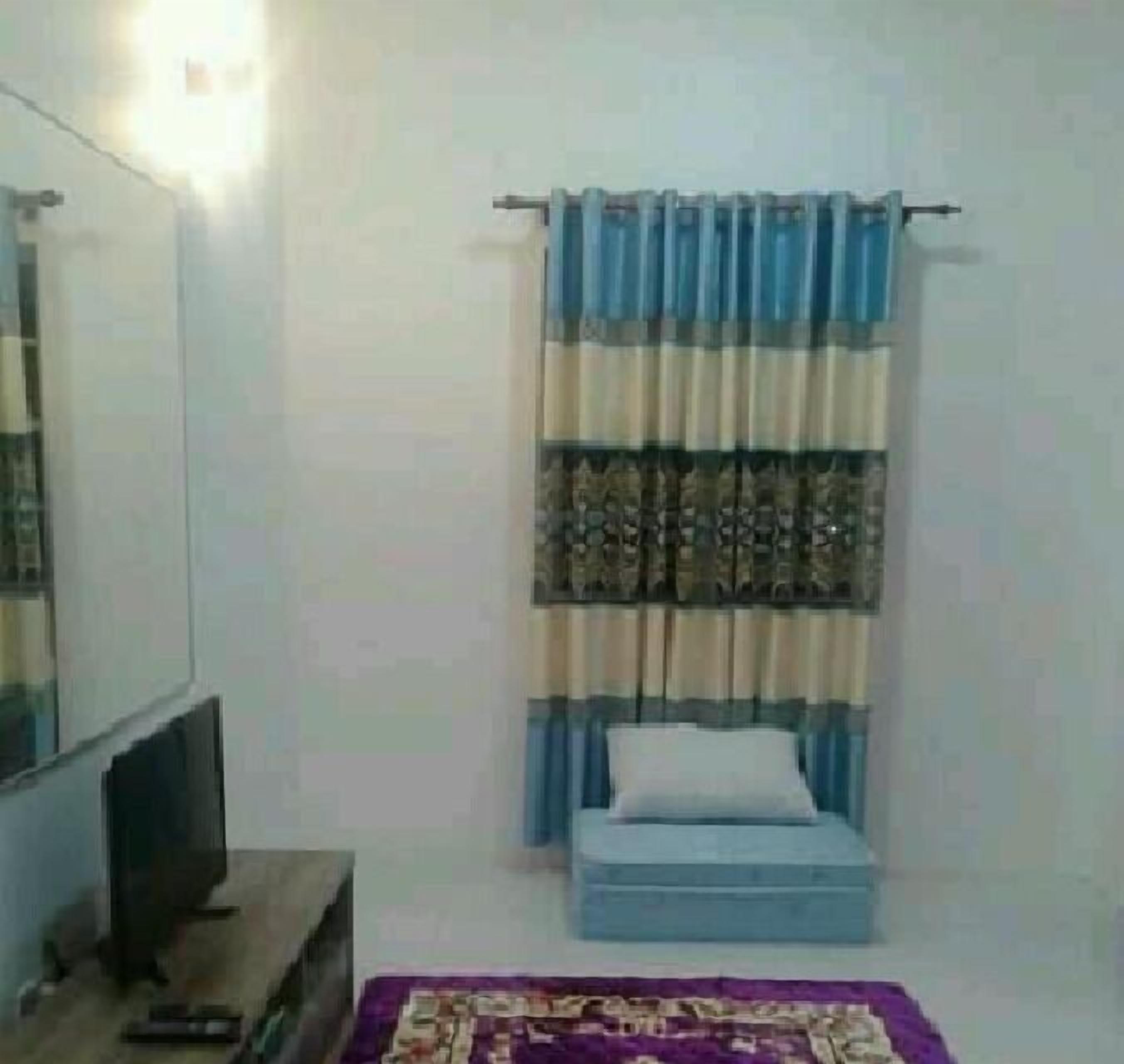 Une chambre à coucher avec un lit, un téléviseur posé sur un meuble et une fenêtre avec des rideaux.
