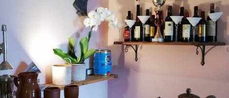 A kitchen counter with a variety of items including a teapot, cups, a pitcher, and a shelf with bottles and a trophy.