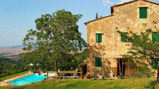 Um edifício rústico de pedra com piscina, rodeado por vegetação exuberante e uma vista clara do campo.