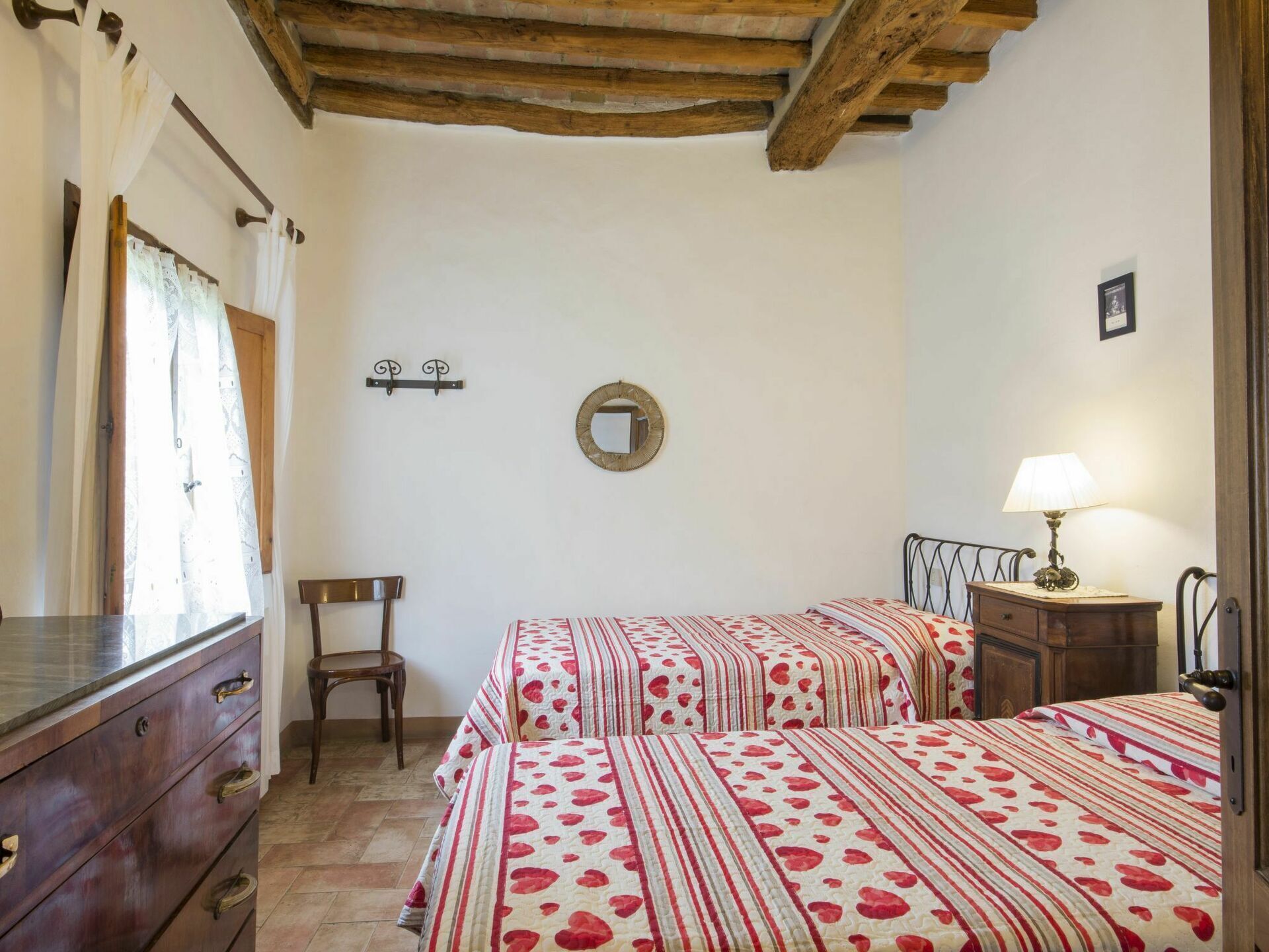 Une chambre avec deux lits, une commode en bois, une chaise, un miroir et une lampe.