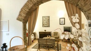 Uma sala de estar aconchegante com um arco de tijolos, móveis de vime, uma televisão e objetos decorativos.