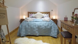 Une chambre à coucher comprenant un lit, deux tables de chevet, une commode en bois, un miroir et un sac à linge suspendu.