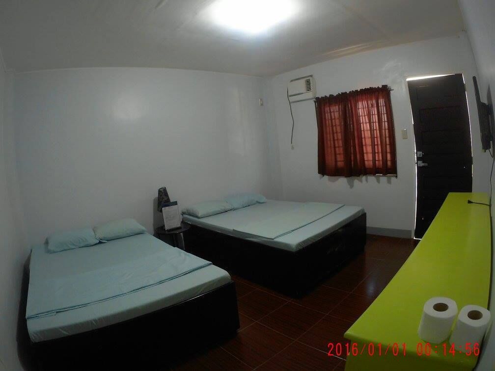 A room with two single beds, a small table with a green top, and a door with a red curtain.