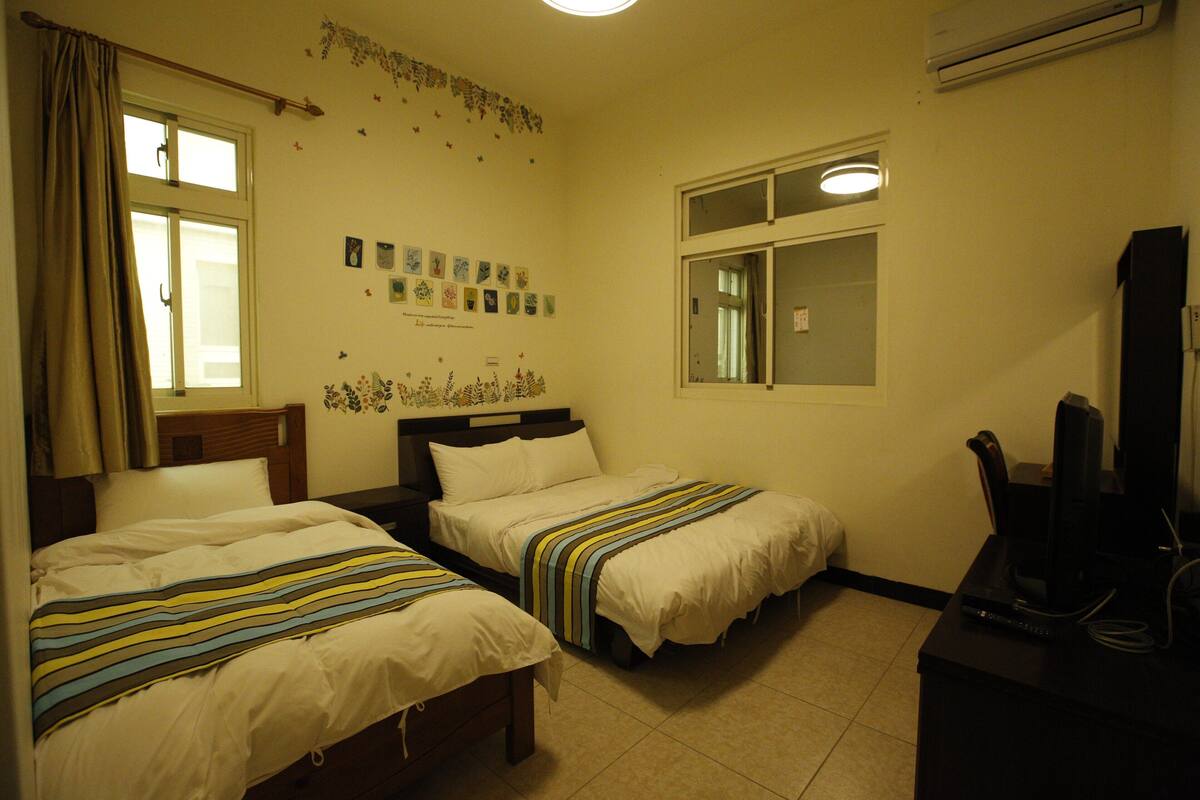 A hotel room with two beds, a desk with a computer, and a window with curtains.