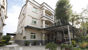 A multi-story residential building with a covered entrance, potted plants, and a small garden area. - Hai Bin Minsu (Jinning)