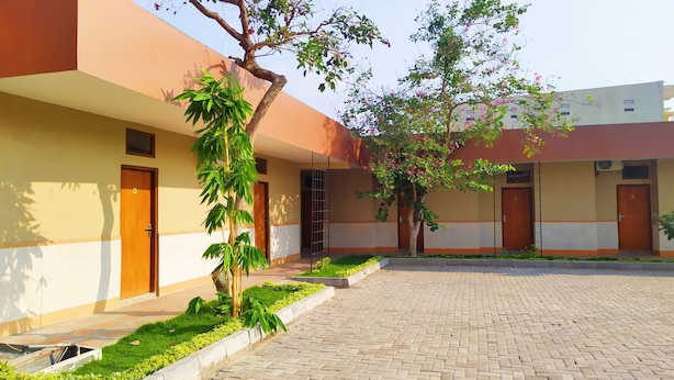 A courtyard with a paved walkway, a bamboo plant, and a tree with pink flowers. - Griya Alisha (Sleman)
