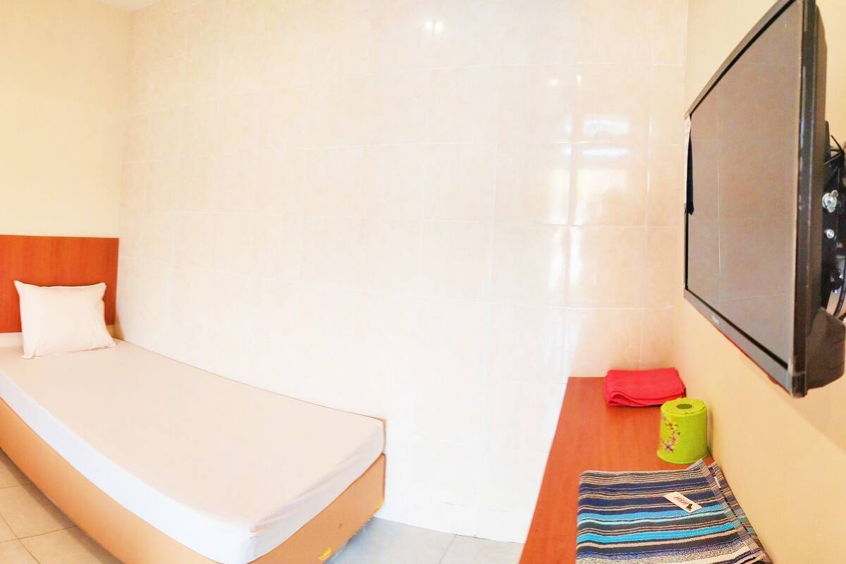 A hotel room with two beds, a wooden headboard, a TV, and a small table with a towel and a green bottle.