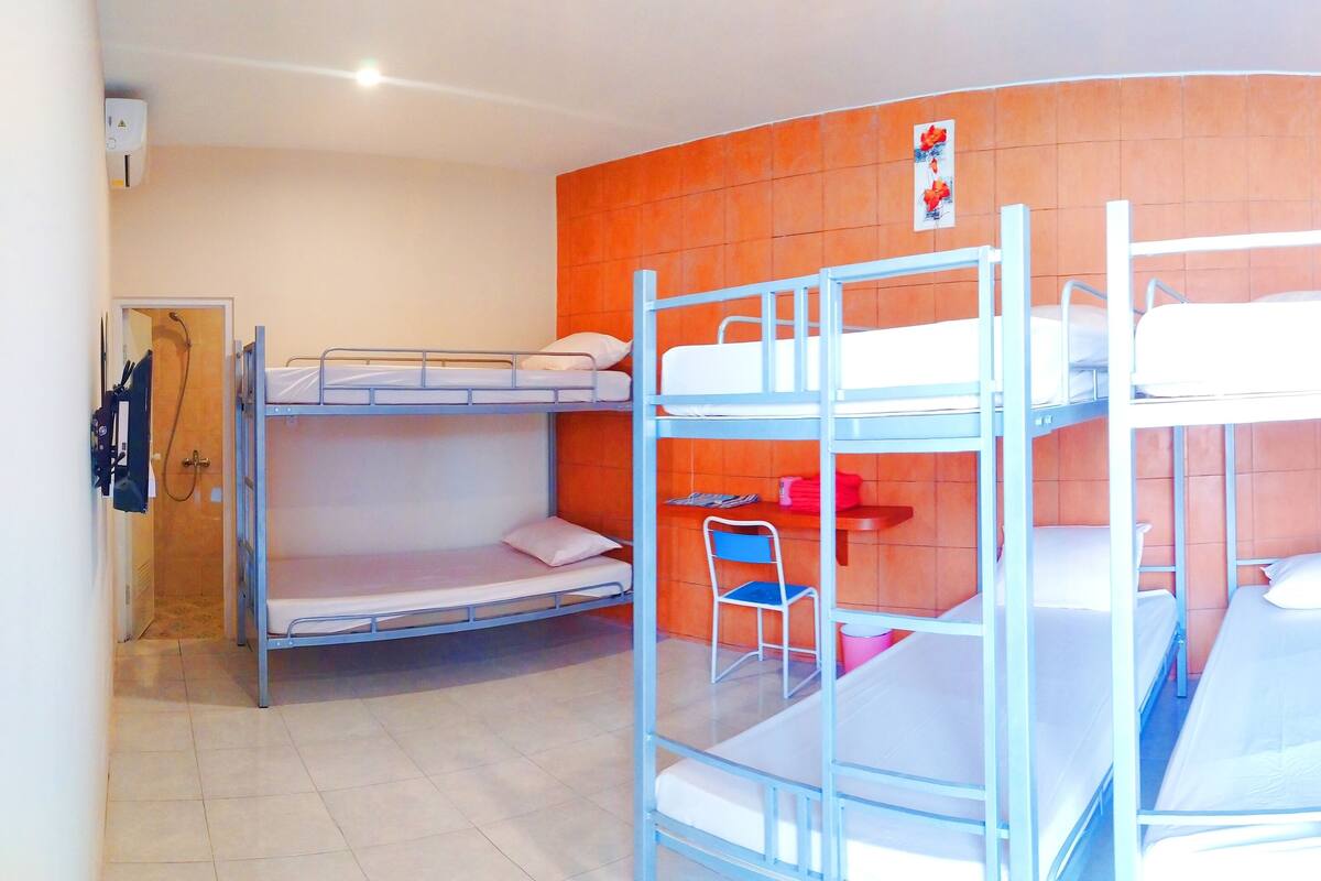 A dormitory room with bunk beds, a chair, and a small table.