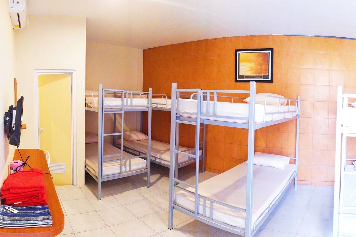 A dormitory room with bunk beds, a bedside table, a chair, and a painting on the wall.