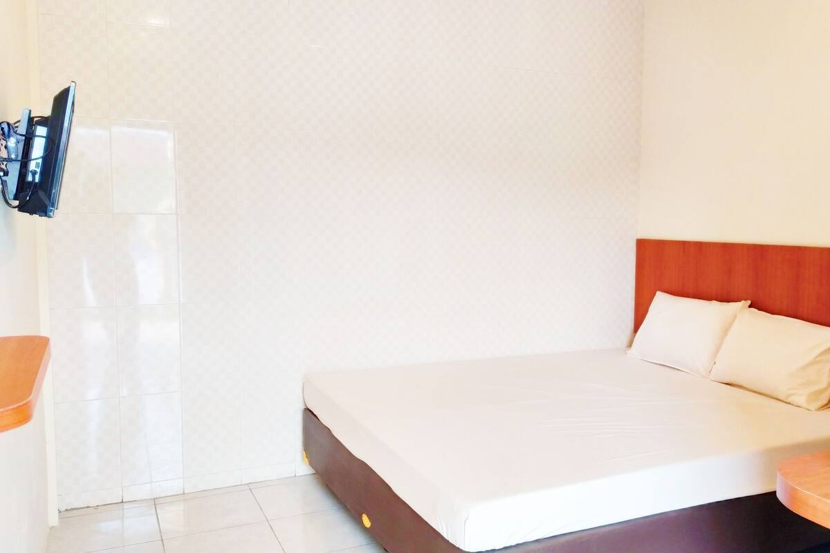 A hotel room with a bed, a wooden headboard, a painting on the wall, and a TV mounted on the wall.