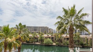 A resort with a pool, palm trees, and modern buildings in the background. - 308 Juliette on the Waterfront Marina (Cape Town)