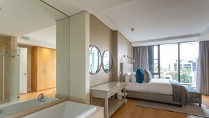 A modern hotel room with a large bed, a sitting area, a bathtub, and a large window with a city view. - 308 Juliette on the Waterfront Marina (Cape Town)