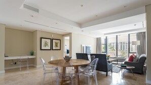 A spacious living area with a dining table, clear chairs, a sofa, and a view of the city through large windows. - 308 Juliette on the Waterfront Marina (Cape Town)