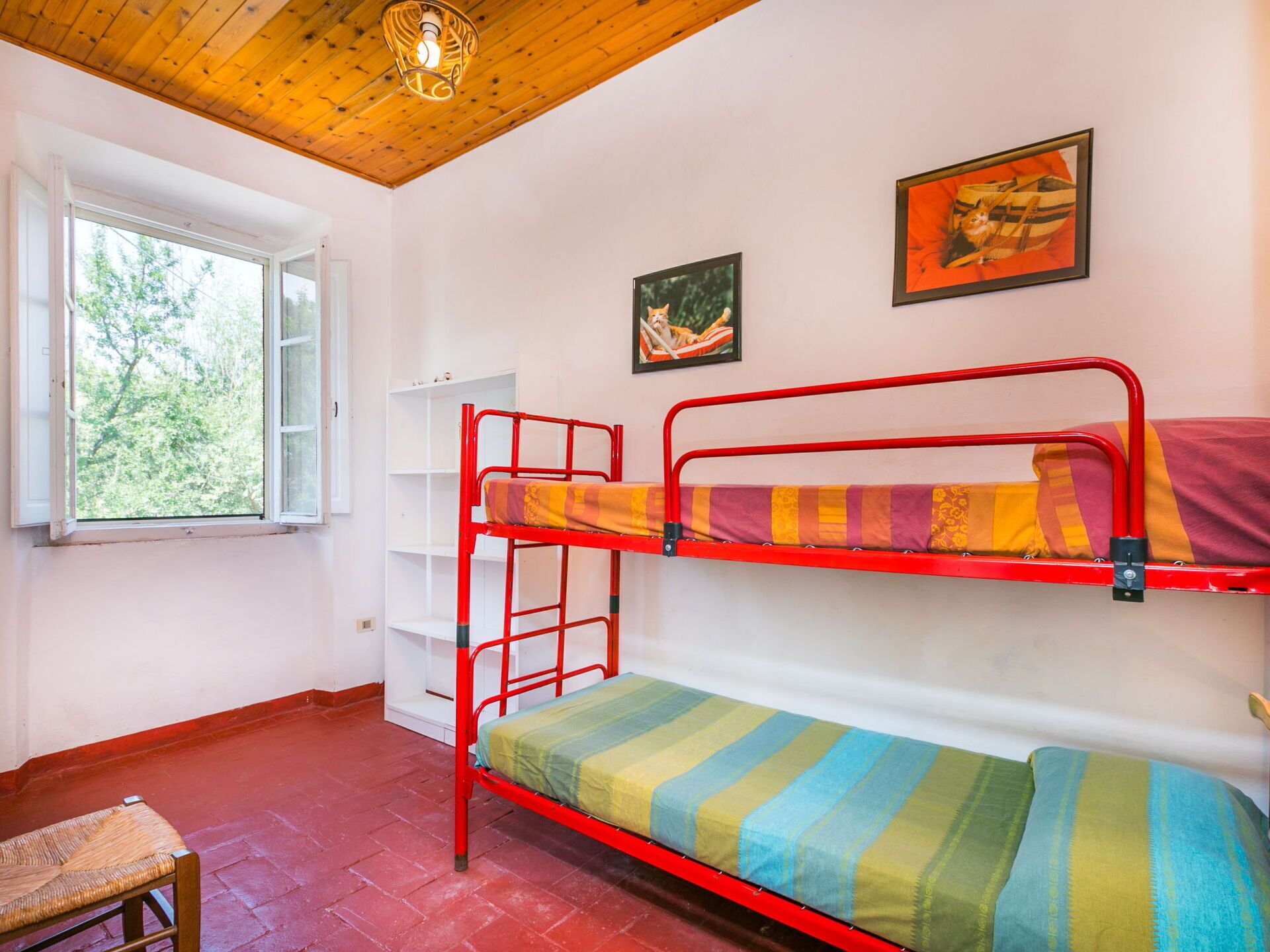 Camera con letto a castello, finestra, soffitto in legno e due quadri appesi al muro.