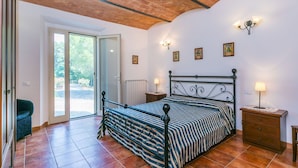 A bedroom with a bed, a nightstand, a lamp, a chair, and a door leading to a balcony. - Nice apartment in villa for 17 people with pool, TV and pets allowed (Rosignano Solvay-castiglioncello)
