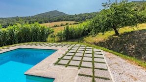 A swimming pool with a surrounding stone deck and grass inlay, set against a backdrop of lush green hills and a clear sky. - Nice apartment in villa for 17 people with pool, TV and pets allowed (Rosignano Solvay-castiglioncello)