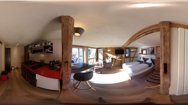 Een moderne keuken met een gebogen eiland, een eethoek met een houten tafel, en een knus slaapkamer met een bed en een groot raam.