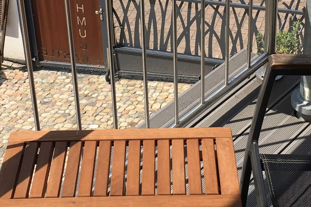 Een houten bank, metalen hekwerk en een poort met 'HOMESPOON' gegraveerd.