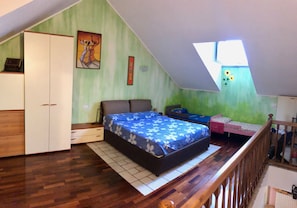 A bedroom with a sloped ceiling, a bed with a floral bedspread, a wardrobe, a small desk, and a window with a view of the sky. - The Bellavista -the lake maggiore from your balcony (Meina)